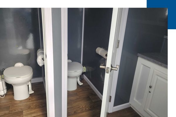 Interior view of a luxury restroom trailer featuring wood-style flooring, white cabinetry, and private stalls with standard flushing toilets and modern hardware.