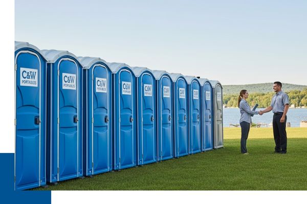 A representative from C&W Portables shaking hands with a client in front of a long, orderly row of clean blue porta johns at a lakeside event venue.