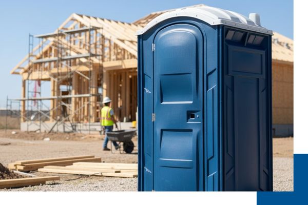 A clean, dark blue portable restroom unit placed on a gravel driveway at a residential home construction site with a worker in the background.