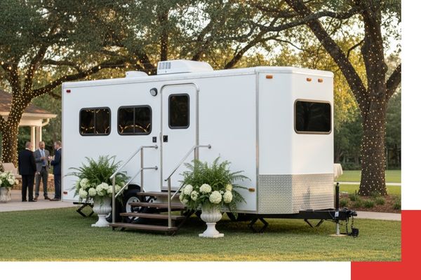 A clean, white luxury mobile restroom trailer parked on a lush green lawn at an outdoor wedding venue.