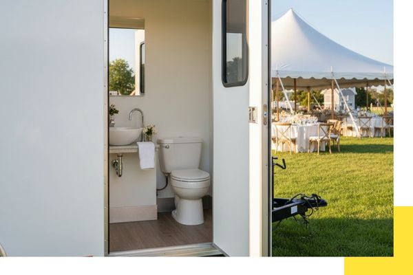 restroom trailer parked on grass with event tent in background