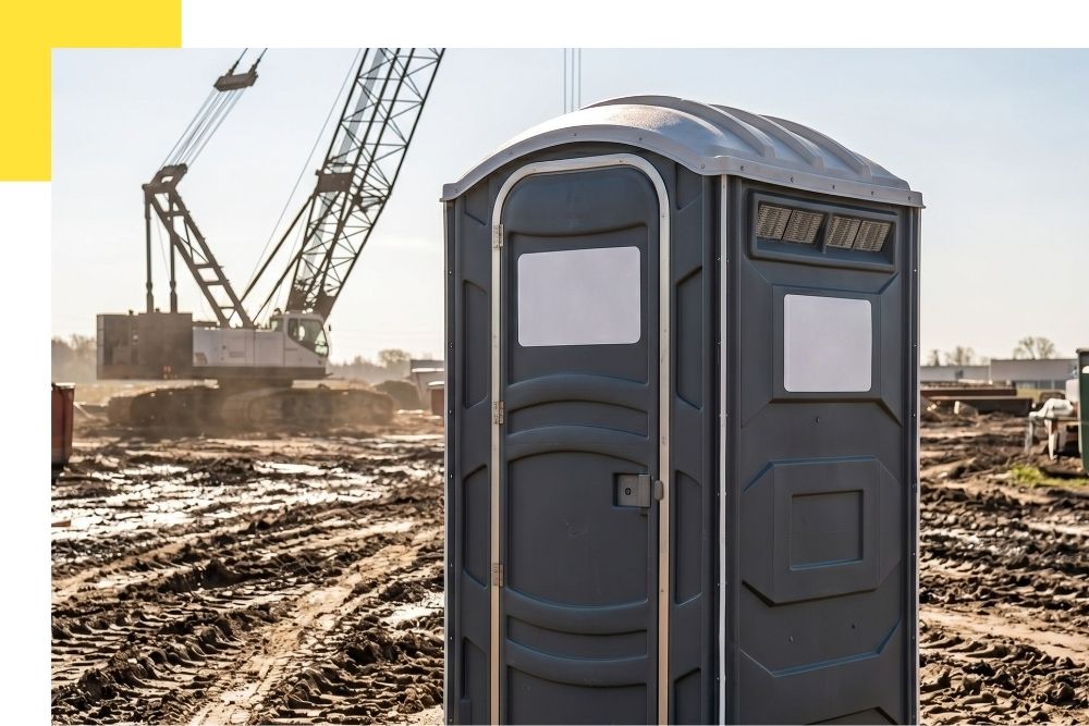 A square stock photo of a clean, deluxe Jons to Go branded porta potty unit set up in a lush park in Bravo, Michigan, with a summer event tent and colorful banners visible in the background.