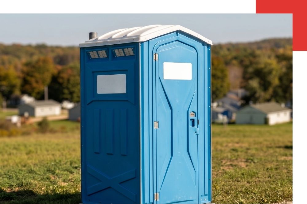 close-up photograph of a clean, blue portable restroom unit featuring the 'Millikin Portables' logo, sitting on grass next to a gravel path in Johannesburg, Michigan.
